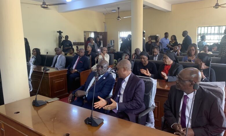 A courtroom scene with attendees seated, some listening intently with focused expressions.