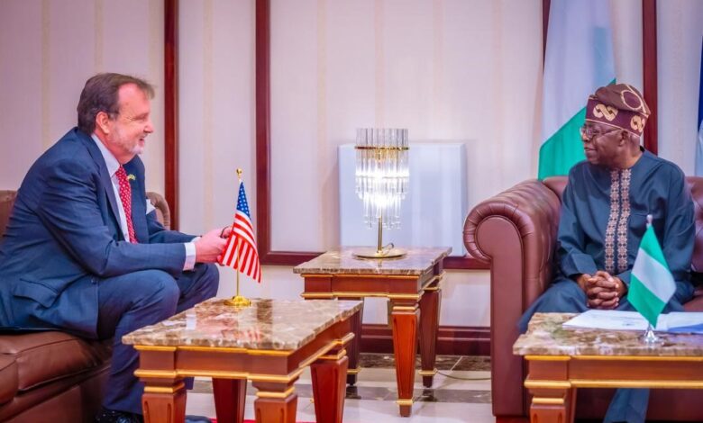 Two men smiling as one presents a small American flag on a desk; elegant room setting with national flags.