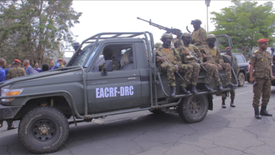 A military vehicle with soldiers onboard and others standing beside, labeled "EACRF-DRC."