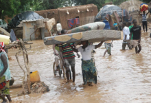 People wade through a flooded area carrying belongings.