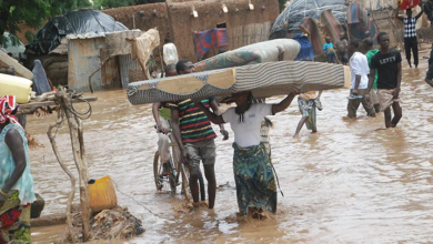 People wade through a flooded area carrying belongings.