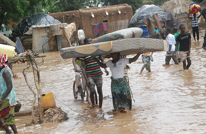 People wade through a flooded area carrying belongings.