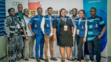 Group of smiling people wearing matching vests and ID badges in front of a "Ghana Fact-Check" banner.