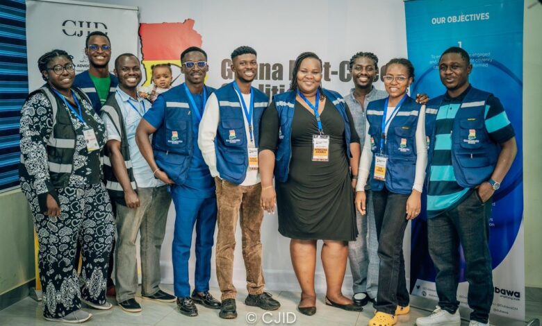 Group of smiling people wearing matching vests and ID badges in front of a "Ghana Fact-Check" banner.