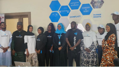 Group of individuals in branded t-shirts standing in front of a wall with hexagonal designs about social issues.