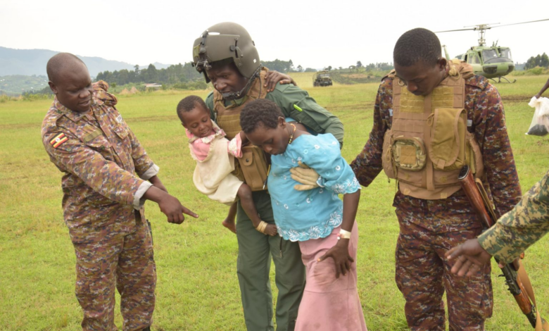 Soldiers assisting a woman and child in a grassy field with a helicopter in the background.