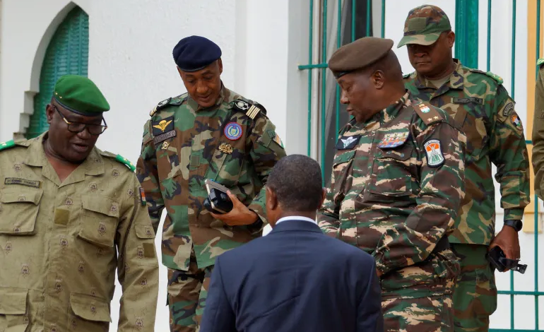 Four military officers in camo uniforms talking with a man in a suit, outdoors near a building.