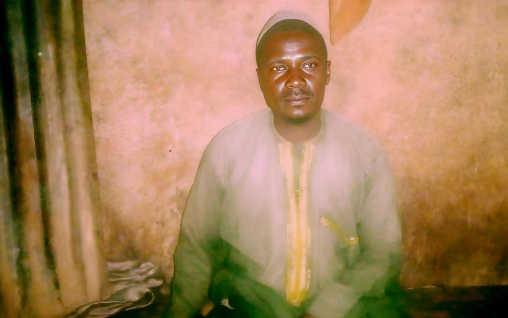 Man in traditional attire posing for a portrait against a textured background.