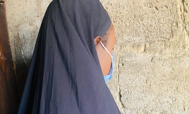 Person in a dark veil leaning against a textured wall, partially facing away.