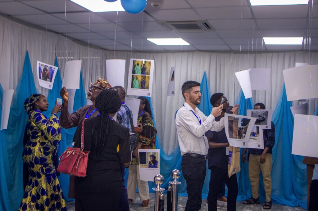 People viewing photos at an exhibition with blue and white drapes.