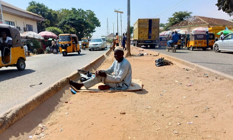 Man sitting on a roadside median with passing traffic and auto rickshaws in a busy street scene.