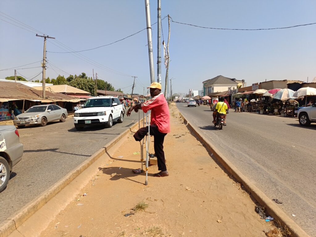 Person leaning against a pole by a busy street with cars and a market in the background.