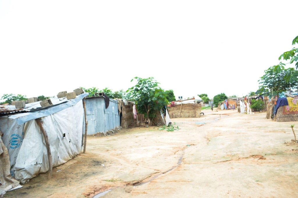 Rustic village path with makeshift shacks and clothes drying outside.