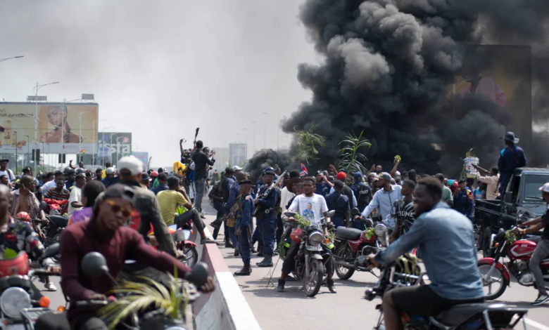 Crowd on motorcycles amidst protest, with people raising hands and black smoke in the background.