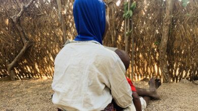 Deborah Salama sitting in her compound at Luran Village, carrying her youngest child in her arms.