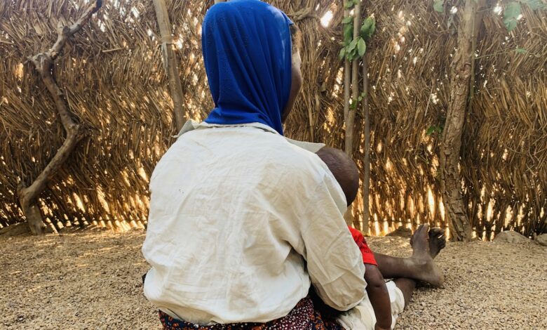 Deborah Salama sitting in her compound at Luran Village, carrying her youngest child in her arms.