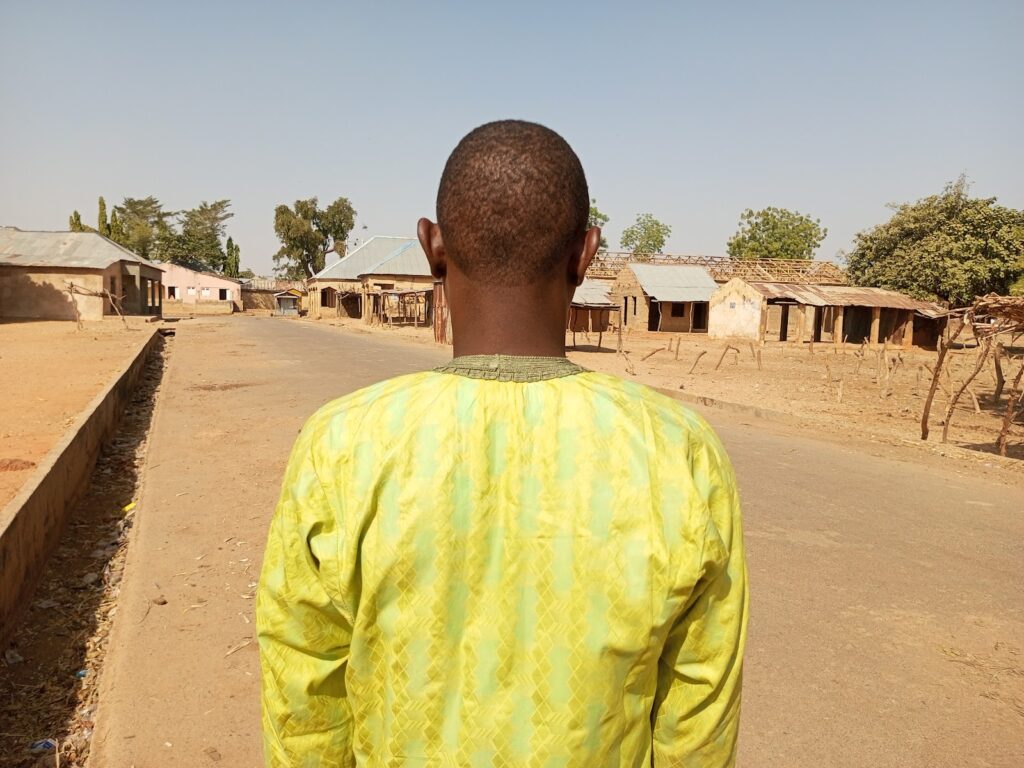 Person in a bright yellow outfit walking down a deserted village street under a clear blue sky.