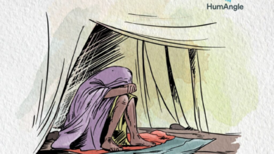 A person sits wrapped in a cloth inside a tent, with their head resting on their knees, conveying a sense of solitude and contemplation.