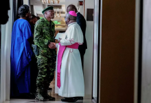 A soldier and a religious leader in conversation, surrounded by others, in a hallway.