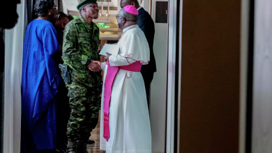 A soldier and a religious leader in conversation, surrounded by others, in a hallway.