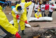 Emergency workers in yellow protective suits dig through debris while others in white vests observe, with a stretcher in the background.