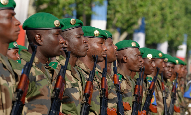 Soldiers in green berets and camo uniforms stand in formation, holding rifles, with trees in the background.