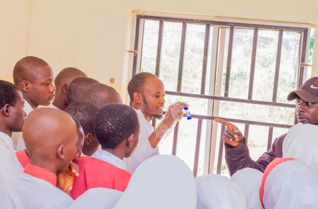 Group of students attentively watch a teacher demonstrating a science experiment with a test tube in a classroom.