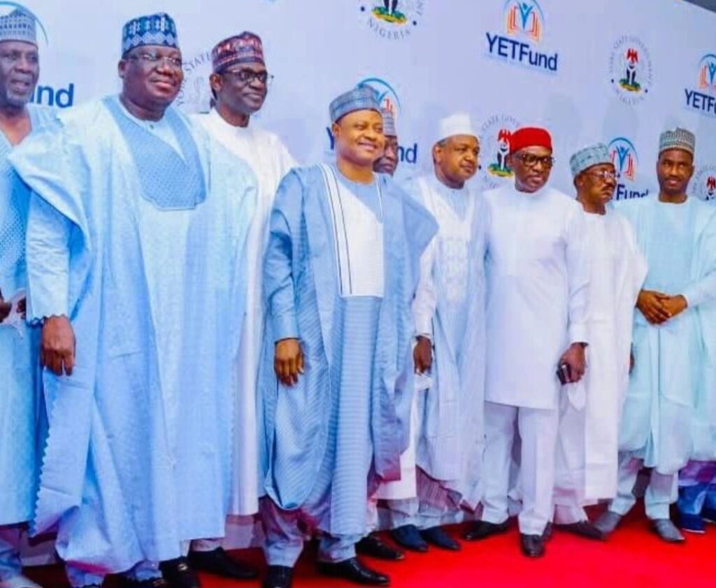 A group of men in traditional attire posing on a red carpet at an event with a YETFund backdrop.