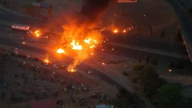 Aerial view of a large fire on a highway at night, with vehicles nearby and dark smoke rising into the sky.