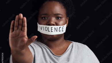 Person with tape labeled "violence" over mouth, holding hand out in a stop gesture against a dark background.