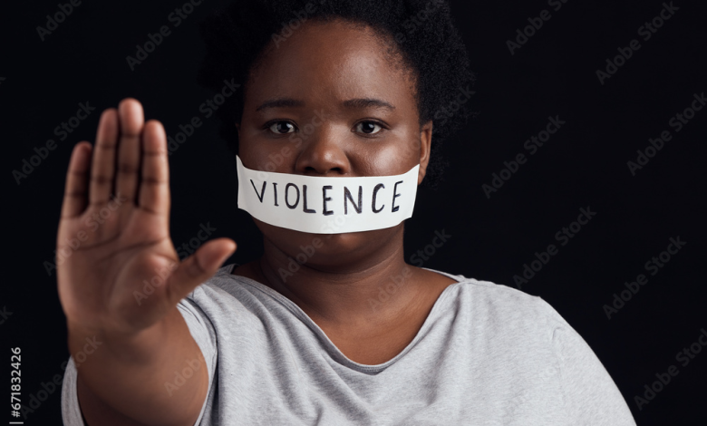 Person with tape labeled "violence" over mouth, holding hand out in a stop gesture against a dark background.