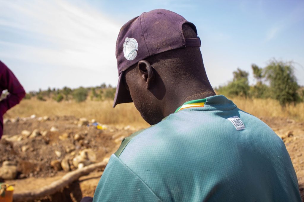 Person in a green shirt and cap facing a dry, grassy landscape under a blue sky.