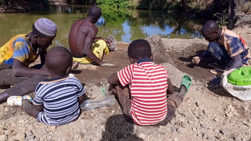 People sitting by a riverbank sorting through sand and gravel.