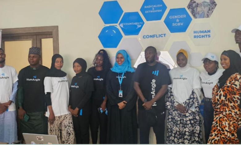 A group of people in "HumAngle" shirts stand together in front of a wall with words like "accountability" and "human rights" on hexagonal tiles.