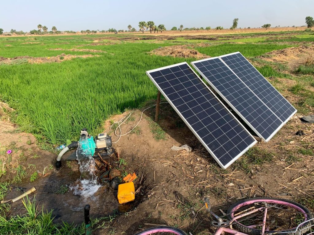 Solar panels power a water pump in a green field, with a bicycle parked nearby.