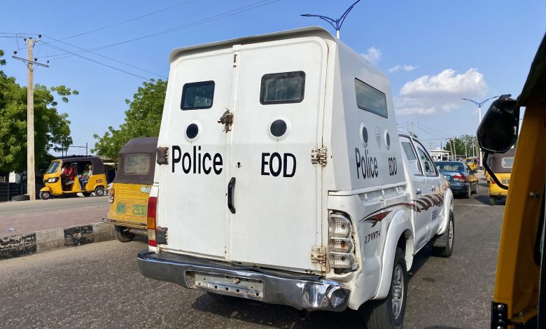 White police EOD vehicle on a busy street with tuk-tuks and cars, trees and a blue sky in the background.