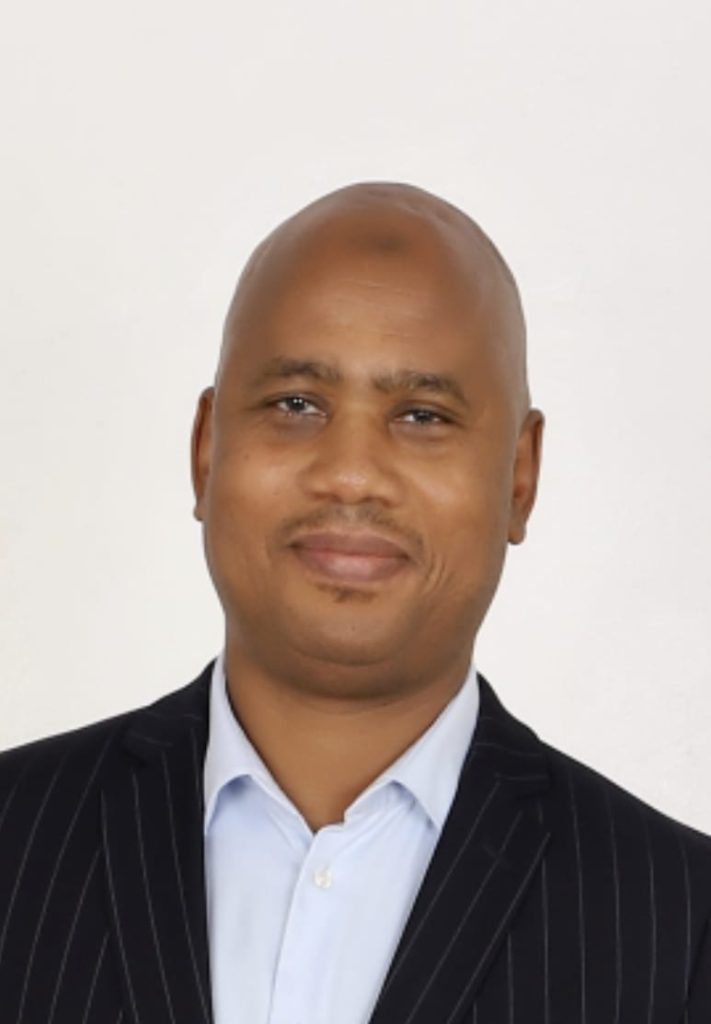 A smiling person in a pinstripe suit and white shirt against a plain light background.