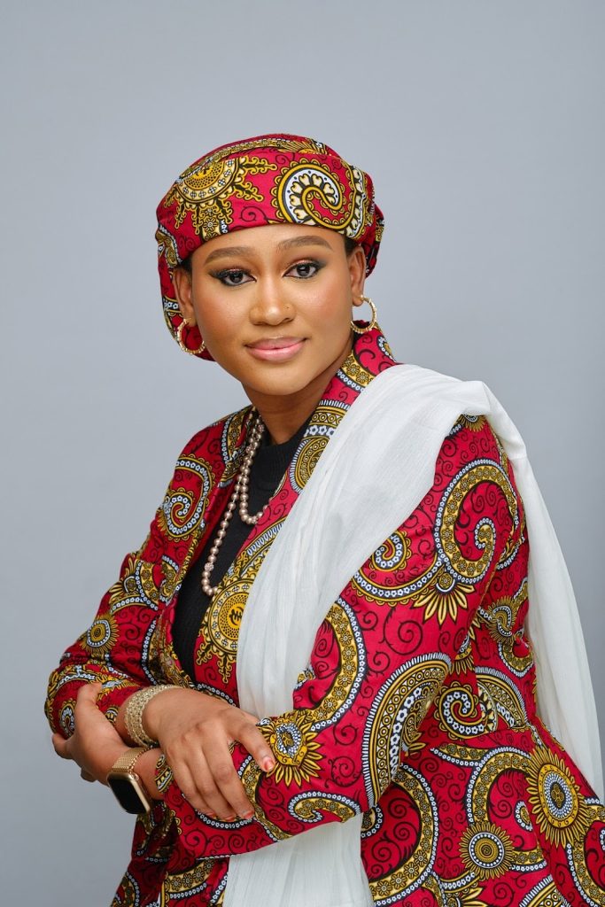 Person wearing a colorful patterned outfit and headscarf with a white shawl draped over their shoulder.