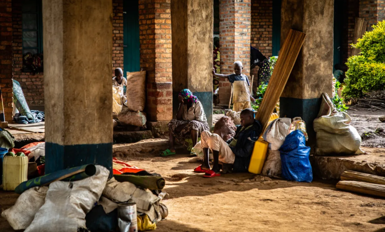 People sitting and standing with bags and bundles in a brick building's corridor, in warm sunlight.