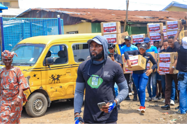 A group of people distribute boxes labeled "Gift a Smile" near a yellow van, with one person leading holding a phone.