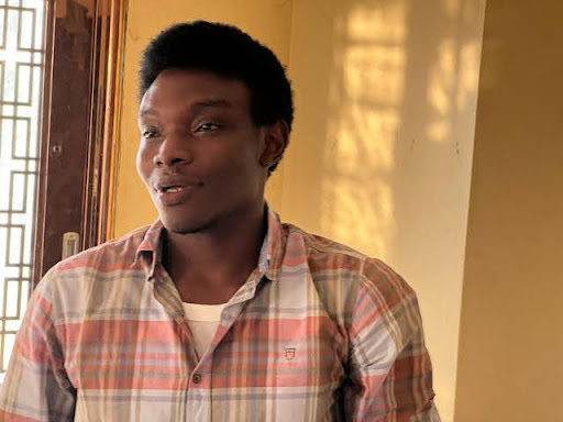 A person in a plaid shirt standing near a window with sunlight streaming in, casting patterns on the wall.
