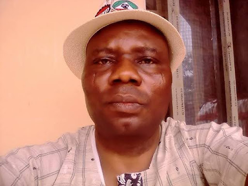Man in a white hat and patterned shirt sits in front of a window with a neutral expression.