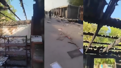 Burnt market stalls with charred roofs and debris scattered on the ground; people visible in the background.