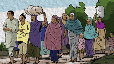 A diverse group of people, including children, walk along a path carrying bundles, with trees in the background.
