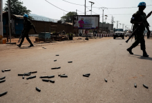 UN soldiers patrol a street with scattered bullet casings in an urban area.