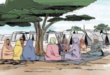 A group of people in colorful clothing sit under a tree near tents, engaging in conversation.