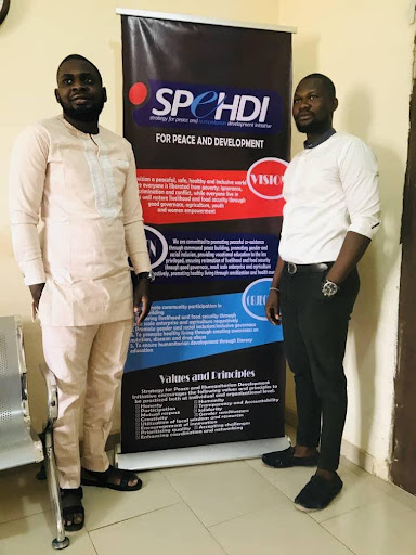 Two men stand next to a banner about peace and development in an indoor setting.