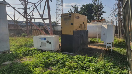 Outdoor generators and equipment surrounded by greenery near a metal tower.