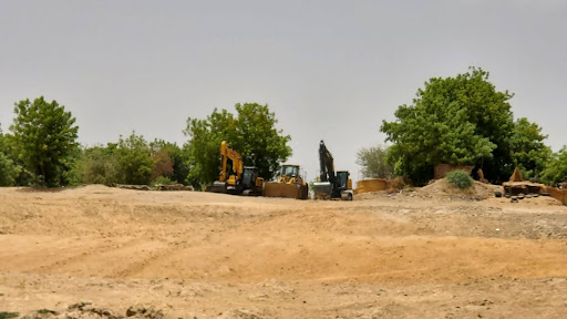 Construction equipment on a dirt clearing surrounded by trees under a cloudy sky.