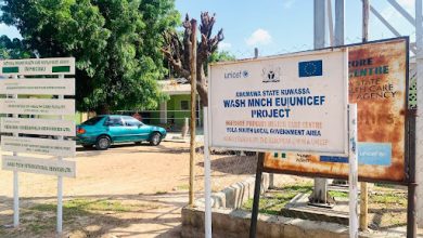Signs for a UNICEF project in a rural area, with a blue car and trees in the background, promoting health initiatives.